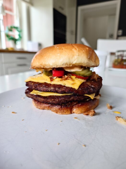 Dubbel hamburgare med ost, karamelliserad lök, picklad chili, smörgåsgurka och dressing på en tallrik i hemmamiljö.