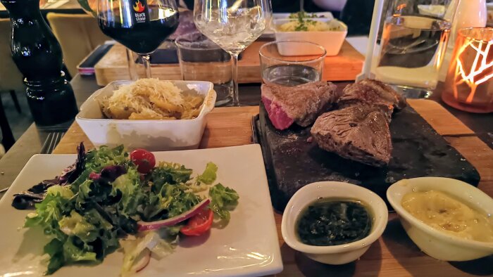 Tallrik med sallad, kött på het sten, såser och bakad potatis med ost på restaurang Blackstone i Falun. Vin och vatten i glas.