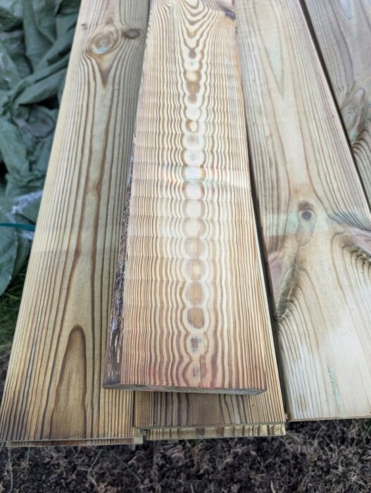 Träbrädor staplade på varandra med synliga årsmönster och ojämnheter; några ser slitna ut på ena sidan.