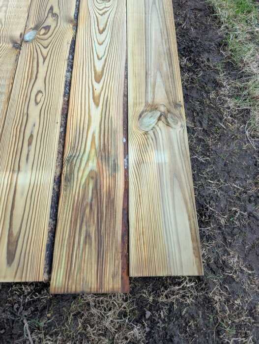 Brädor av premiumtrall med synliga färgvariationer och kvistar, liggandes på marken.