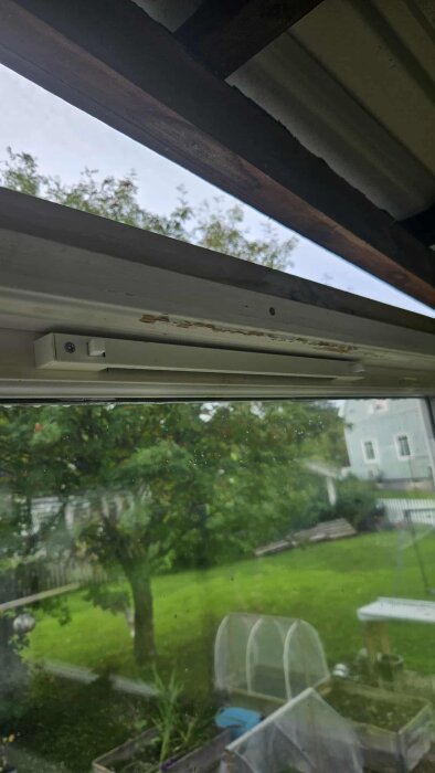 Fönster monterat vid altan med utsikt över trädgård, grön gräsmatta och träd.