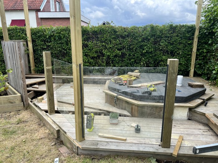 Badtunna under konstruktion med glasräcke och trästolpar på en altan, verktyg och material utspridda.