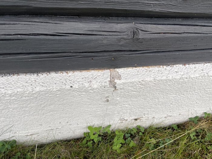 Sprickor i det vita putsskiktet på en timmerstugas grund, målat 1989. Knuttimrad stuga från 1945, delvis på berg.