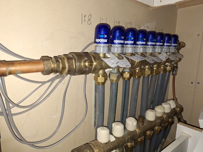 Fördelare för vattenburen golvvärme med Uponor-styrdon i ett köksskåp, flera rör och ventiler synliga.