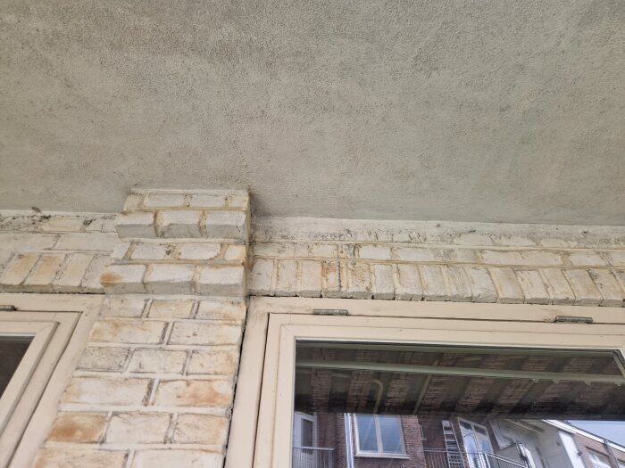 Tegelfasad över fönster på gammal byggnad från 1927 med vitmålad fönsterram, visar potentiell överliggare bakom teglet.