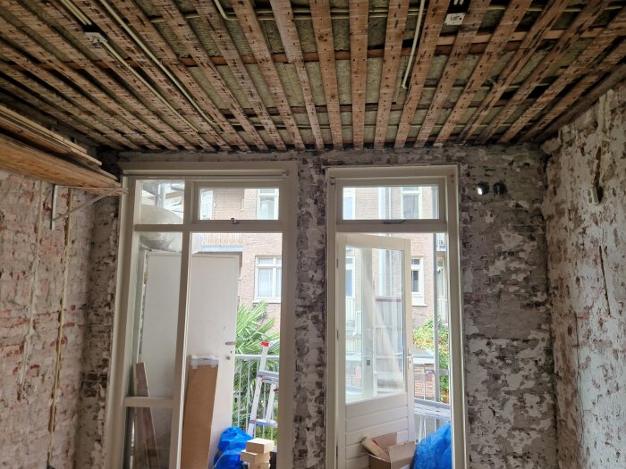 Inre av ett gammalt tegelrum med två stora fönster- och dörröppningar; byggmaterial och verktyg synliga runtom.