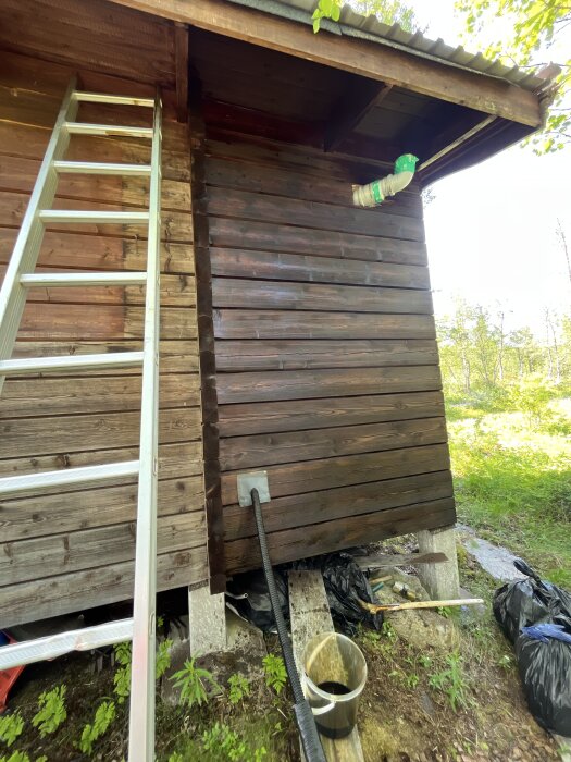 Träfasad målad med egenblandad roslagsmahogny utan pigment. Stege står lutad mot väggen, bredvid syns en hink och pensel på marken.
