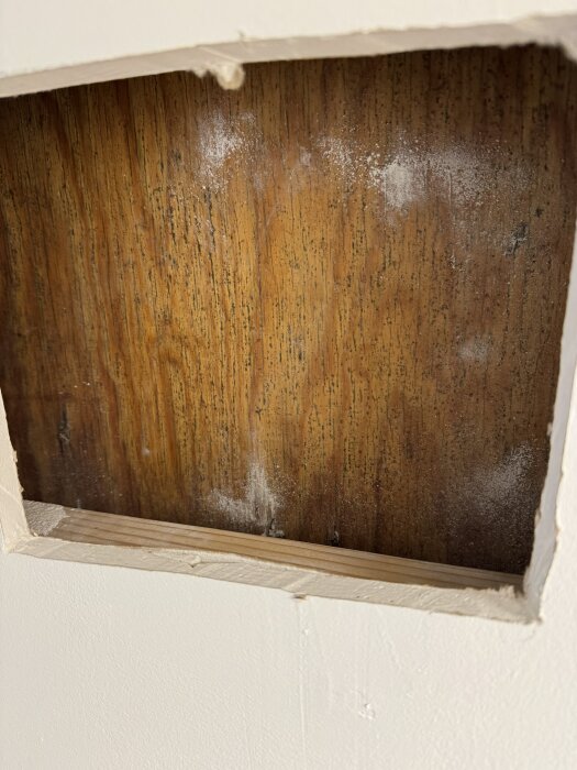 Utsågat hål i vägg visar träpanel med svarta fläckar, möjligtvis mögel. Träet ser kallt och torrt ut, utan synlig väta eller vattenledning.
