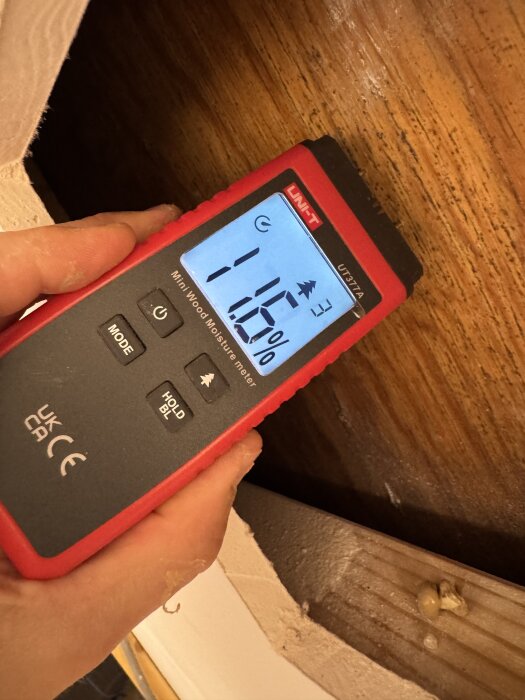 Fuktmätare visar 11,6% på en brun plywoodskiva med svarta fläckar, eventuellt mögel, bakom gips i garderob. Inga vattenledningar synliga.