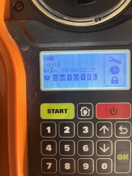 Närbild av en Worx robotgräsklippares kontrollpanel med display som visar tid, datum och symboler. Tangentbord med siffror och knappar för start och stopp.