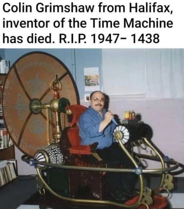 Man i blå skjorta sitter på en hemgjord tidsmaskinsstol med stora kugghjul och mässingsdetaljer i ett rum med hylla och affisch på väggen.