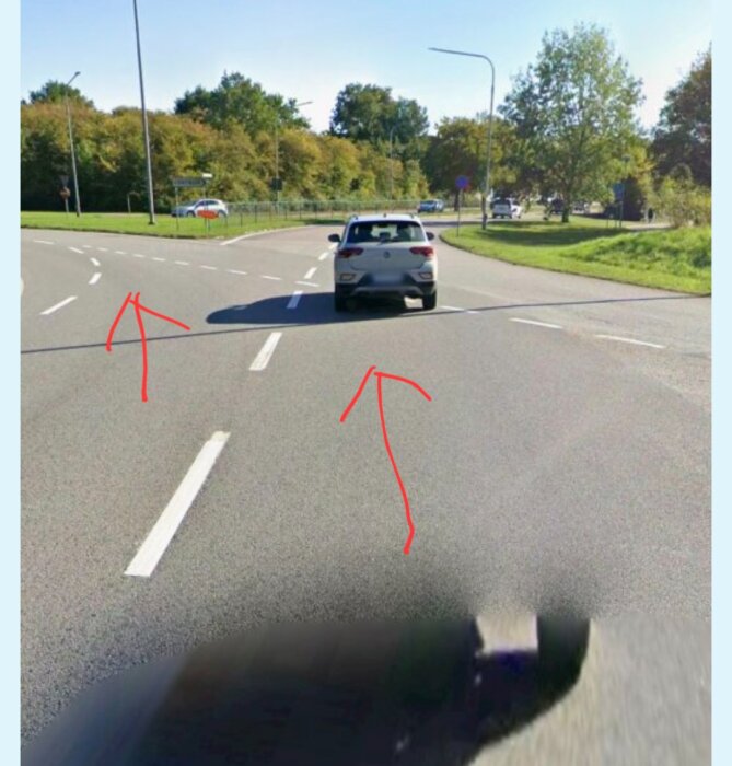 Bil på väg in i cirkulationsplats med flera vita vägmarkeringar och röda pilar som visar möjliga körbanor.