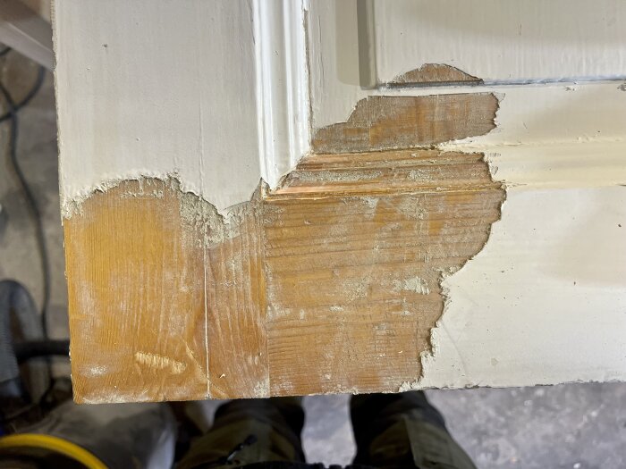 Färgborttagning med varmluftspistol på träram, delvis avlägsnad färg visar träytan.