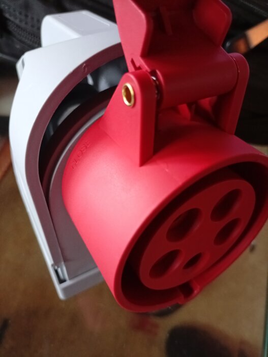 Röd fempolig byggkontakt för vägginstallation, med ett öppet lock, visas mot en suddig bakgrund.