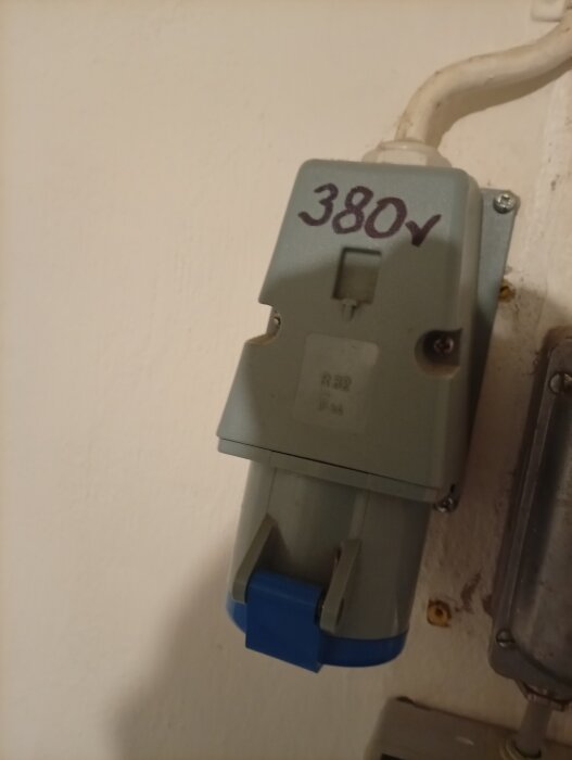 En väggmonterad 380V eluttag med en blå och grå kåpa, förberedd för 4-ledaranslutning, ska bytas mot en 5-ledaranslutning.