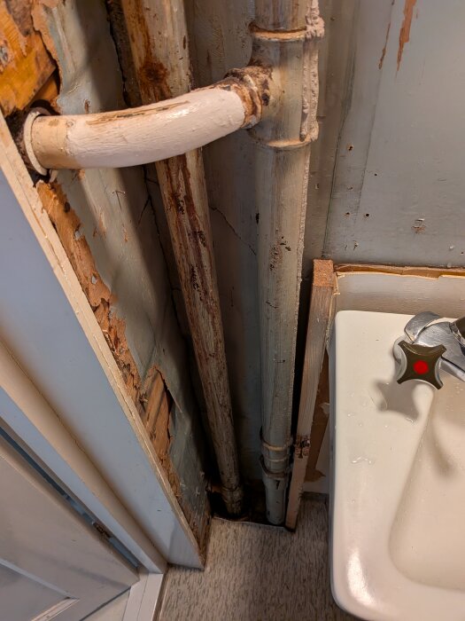 Äldre kopparrör bakom vägg med synliga skador och korrosion nära tvättställ i en pågående renovering av en toalett.