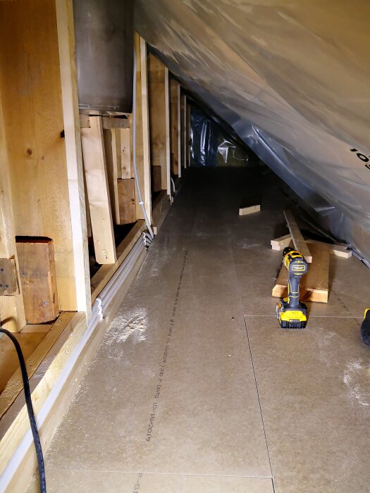 Isolerad vind med ny golvspån och glespanel, en skruvdragare och träbitar ligger på golvet.