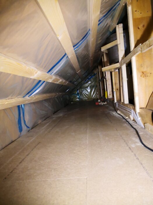 Ett nyrenoverat vindsutrymme med golvspån och gipsskivor, förberett för förvaring av flyttkartonger och vinterkläder.