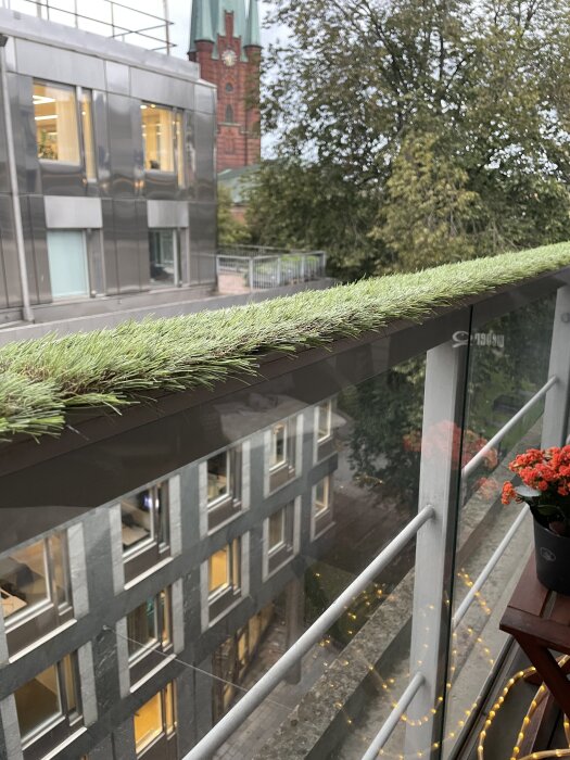 Konstgräs monterat på balkongräcke med bakgrund av byggnad och träd, avsett för att dämpa regndroppar.