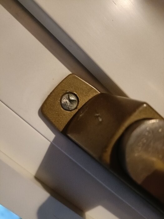 Bronsfärgat handtag på en inglasad balkongdörr med en envägsskruv som sitter fast i handtagets fäste.