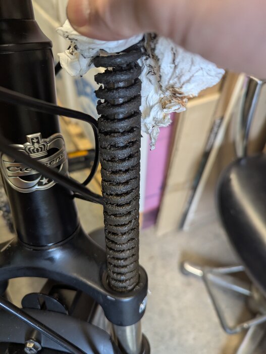 Cykelgaffel med rostig fjäder och papper ovanpå, visas i närbild i ett garage.