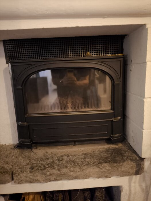 Svart eldstad med glaslucka och stenbänk, del av ett diskussionsforum om byggprojekt, fokus på ventilationsspakar och askhantering.