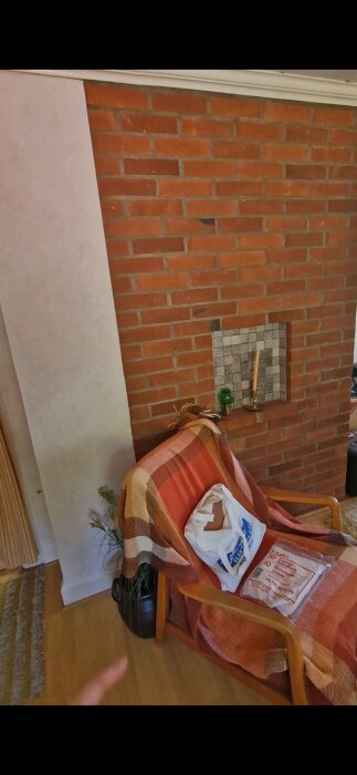 Röd tegelmurstock i rum med filtklädd stol och krukväxt. Muren har en nisch med ljus och ornament.