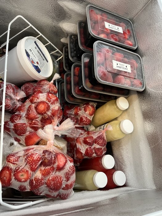 Frys med flera lådor bär, plastpåsar med jordgubbar och flaskor med juice eller dryck.