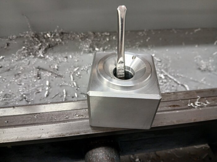 Metallblock med skäroljehållare och metallspån i bakgrunden på en arbetsbänk i garaget.