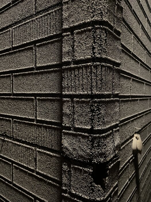 Fasad med skivor som liknar tegel, grov yta med asfalt/tjärpapp, skarv synlig i hörnet. Eventuellt isolerande material baserat på sockerrör.