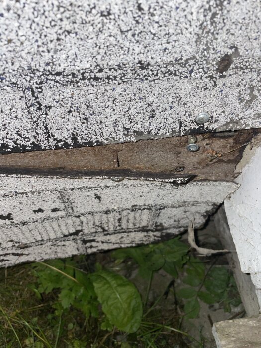 Vägg med fasadskivor som liknar tegel, med grusig yta och skruvar synliga, omgiven av växtlighet och trädetaljer.