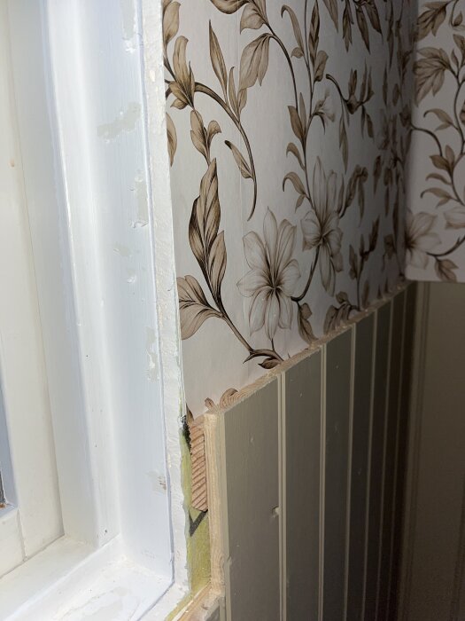 Fönsterkarm med blommig tapet och pärlspontpanel på väggen, visar övergången och limmade reglar för att fästa pärlsponten.