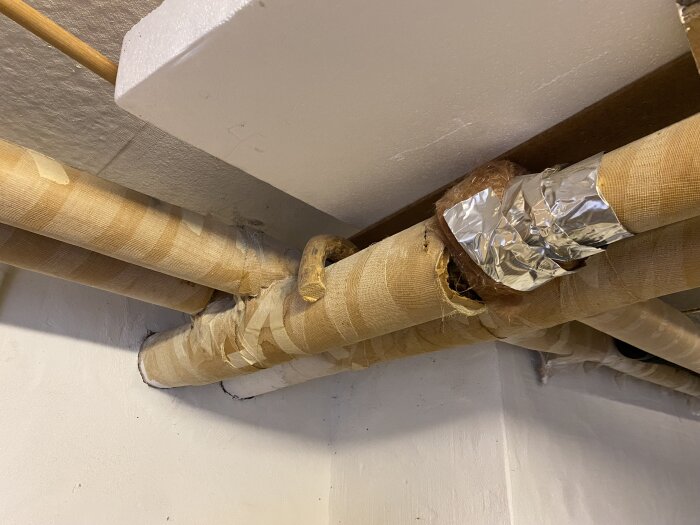 Rör i källartaket med skadad isolering och silvertape, oro för asbest i äldre hus.