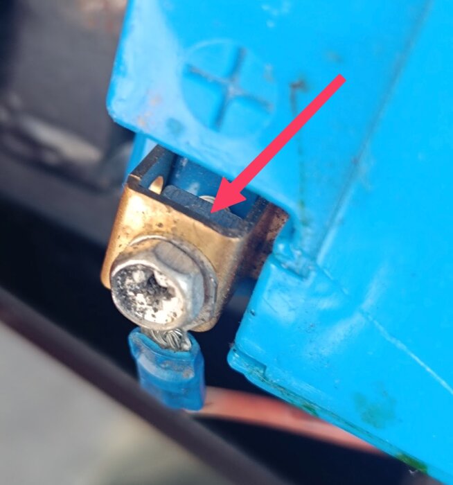 Blå plastdel med metallfäste där en mutter saknas, markerat med röd pil.