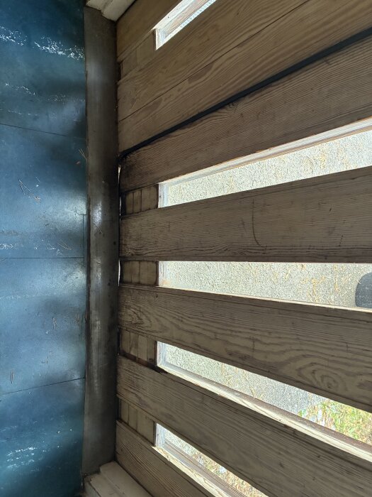 Träytterdörr med genomskinliga insatser och metallkant, delvis böjd med glipor mot karm, sedd från insidan.