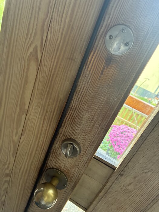 Trädörr med två lås: överst ett tillhållarlås, under ett med vred och nyckelhål, samt en guldfärgad dörrknopp.