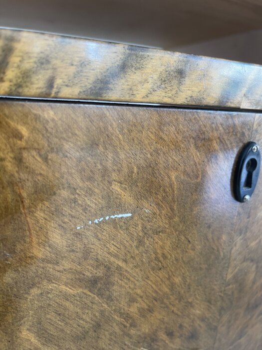 Närbild av en äldre byrå i bonad björk med vitt färgstänk på lådfronten bredvid ett nyckelhål i metall.