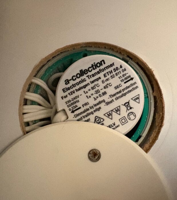 Transformator för 12V halogenlampor, med specifikationer och symboler, monterad i taket med vita kablar.