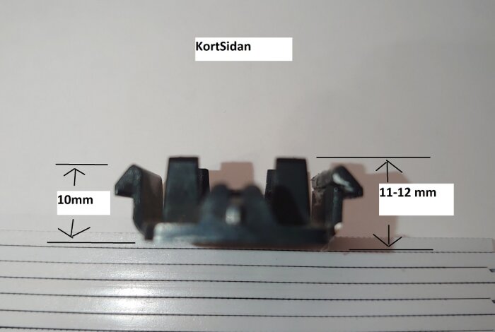 Svart metallclips sett från sidan, med måtten 10 mm på höjden och 11-12 mm på bredden angivna.