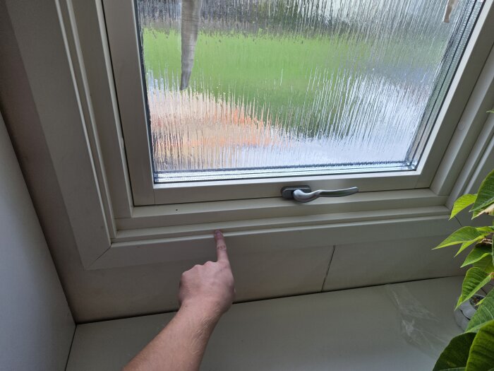 En hand pekar mot kanten av ett fönster med regnvatten utanför, vilket illustrerar en möjlig justering inför en duschinstallation.
