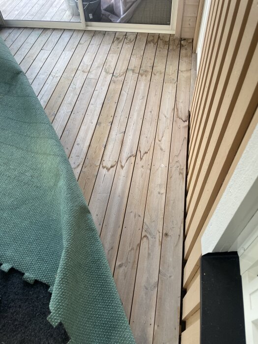 Närbild av oisolerad trätrall i inglasat uterum med del av grön heltäckningsmatta synlig.