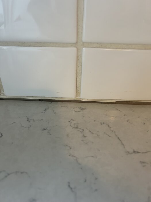 Glipa mellan marmorerad bänkskiva och vit kakelvägg i kök, ett byggprojekt om att fylla ut med fog eller list.