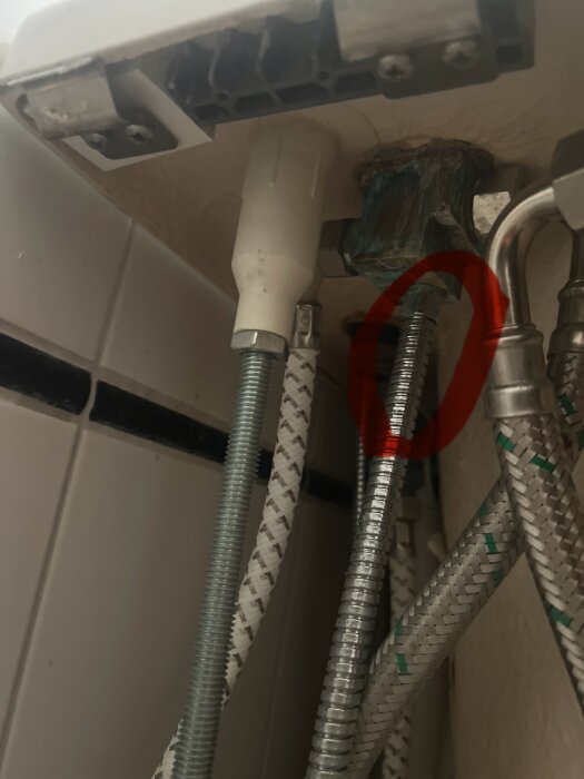 Bild av flera anslutna vattenslangar under en diskbänk eller handfat, en av slangarna är markerad med en röd ring.