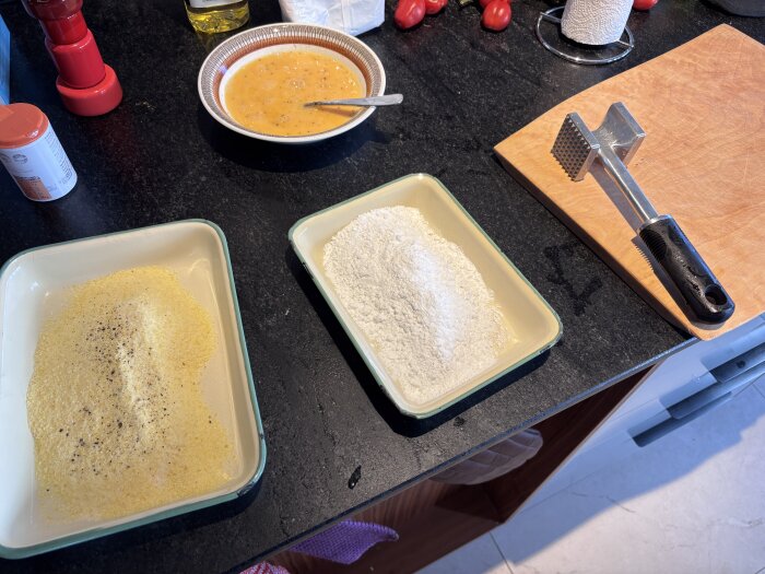 Matlagningsstation med mjöl, brödsmulor, en tallrik ägg, köttbankare och skärbräda; ingredienser för panering.