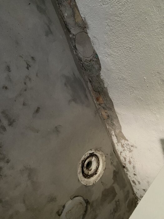 Betongvägg med synlig igensatt hål i hörn och avloppsbrunn i golvet, beskriver plats för potentiell tvättstuga med flytt av avlopp.