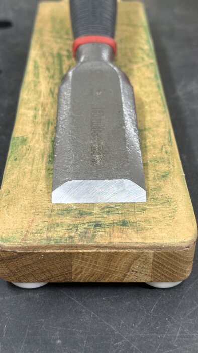 Slipat stämjärn placerat på en trähållare med grönfärgad ovansida.