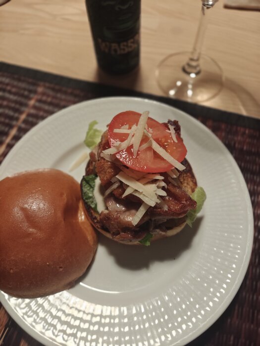 Ceasarburgare med bacon, tomat och ost på en vit tallrik, bredvid ligger en öppen hamburgerbröd.