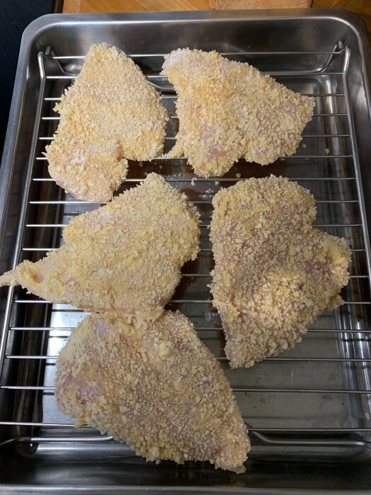 Panerade kycklingschnitzlar på galler, redo för fritering.