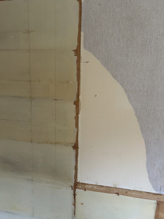 Vägg med avlägsnad vävtapet, synliga skarvar och olikfärgade ytor, delvis exponerad vävtapet och målad yta.