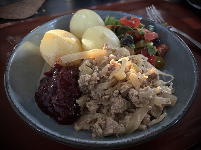 Tallrik med kålpudding, kokt potatis och lingonsylt; serveras med tomat- och salladsröra.